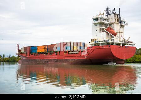 An einem bewölkten Herbsttag segelt ein Containerschiff einen Kanal hinauf Stockfoto