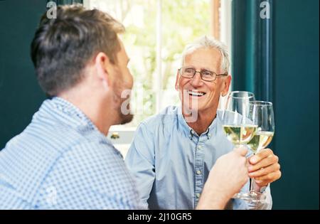Heres zu dir und mir Papa. Aufnahme eines fröhlichen älteren Mannes und seines Sohnes, der zu Hause einen feierlichen Toast mit Weingläsern teilt. Stockfoto