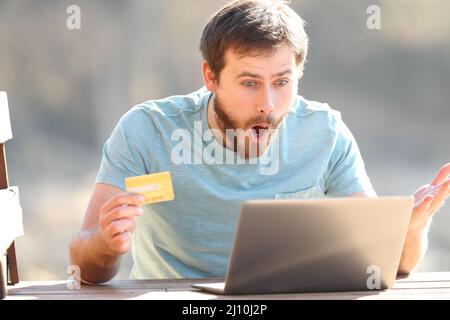 Erstaunlicher Mann, der in der Natur mit einem Laptop und einer Kreditkarte online kauft Stockfoto