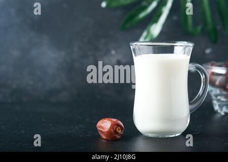 Ramadan Kareem Essen und Getränke. Teller mit Datteln, Glas Milch und Dattelpalmzweig auf schwarzem Hintergrund. Gerechter Muslimischer Lebensstil. Vegetarische Gerichte. S Stockfoto