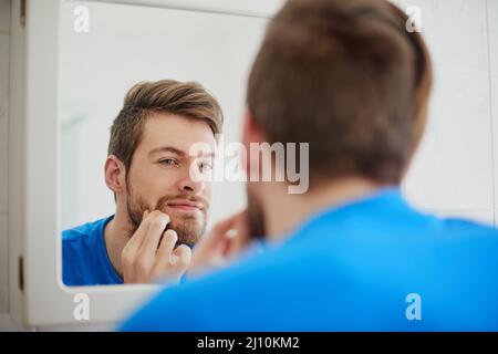 Sollte ich diese Zit zappen oder nicht. Ein kurzer Schuss eines jungen Mannes, der einen Pickel vor einen Badezimmerspiegel quetscht. Stockfoto