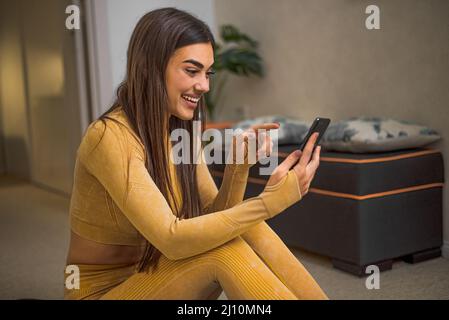 Glückliches, brünett Mädchen, liest ihre Nachrichten, während sie lächelt und ihr Telefon benutzt. Stockfoto