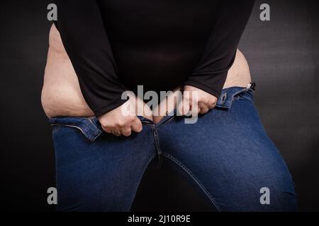 Fette Frau zieht Jeans auf sich selbst auf einem schwarzen Hintergrund Stockfoto