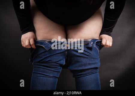 Fette Frau, die auf schwarzem Hintergrund Jeans an den Beinen zieht Stockfoto