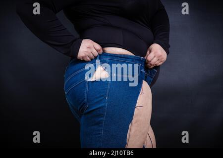 Fette Frau in zerrissenen Jeans auf schwarzem Hintergrund Stockfoto