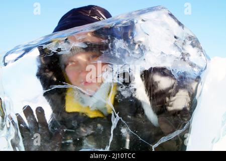 Eine Frau schaut durch eine transparente Eisscholle am Baikalsee Stockfoto