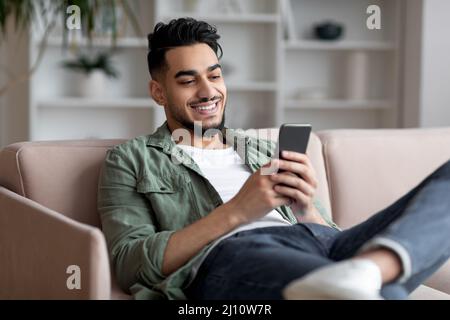 Porträt Des Schönen Jungen Arabischen Kerl Entspannen Mit Smartphone Zu Hause, Stockfoto