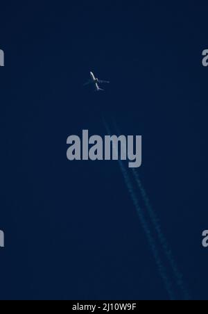 Ein kommerzielles Verkehrsflugzeug in großer Höhe mit Kondensstreifen fährt bei Sonnenuntergang durch einen tiefblauen Himmel. Stockfoto