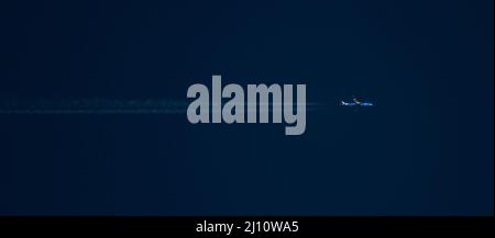 Ein kommerzielles Verkehrsflugzeug in großer Höhe mit Kondensstreifen fährt bei Sonnenuntergang durch einen tiefblauen Himmel. Stockfoto