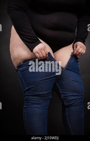 Fette Frau, die auf schwarzem Hintergrund Jeans an den Beinen zieht Stockfoto