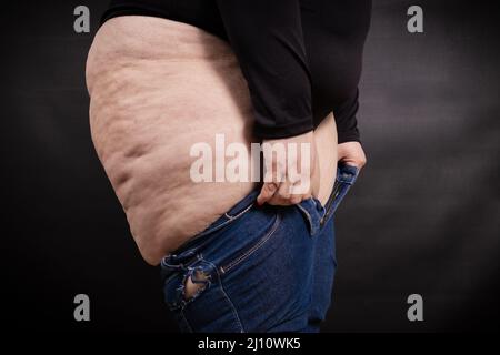 Fat Woman legt Jeans auf sich selbst auf einem schwarzen Hintergrund Stockfoto