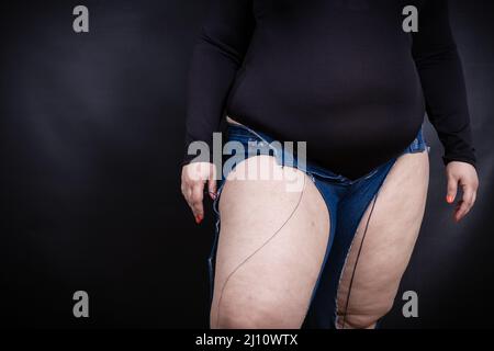 Fette Frau in zerrissenen Jeans auf schwarzem Hintergrund Stockfoto