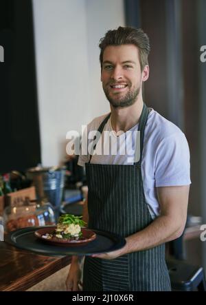 Service mit einem Lächeln. Zugeschnittenes Porträt eines jungen Kellners, der einen Auftrag an einen Kunden übergibt. Stockfoto