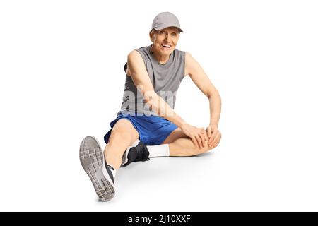 Älterer Mann in Sportkleidung sitzt auf dem Boden und streckt sich isoliert auf weißem Hintergrund Stockfoto
