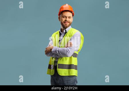Junger männlicher Bauingenieur mit einer Sicherheitsweste und einem Hardhut auf blauem Hintergrund isoliert Stockfoto