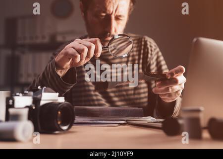 Fotograf, der an seinem Arbeitsplatz einen Negativfilm mit der alten Analogkamera 35 vorführt, selektiver Fokus Stockfoto