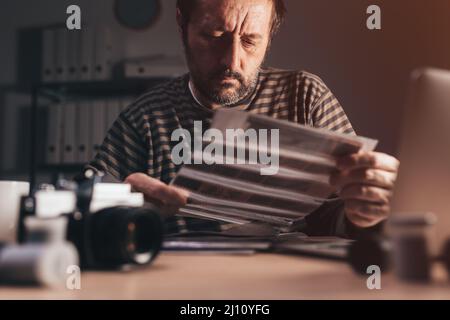 Fotograf, der an seinem Arbeitsplatz einen Negativfilm mit der alten Analogkamera 35 vorführt, selektiver Fokus Stockfoto