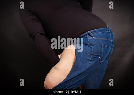 Fette Frau in zerrissenen Jeans auf schwarzem Hintergrund Stockfoto