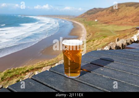 Ein Pint Bier auf einem Tisch mit Blick auf die Rhossili Bay und den Strand auf der Gower Peninsula, Wales Stockfoto
