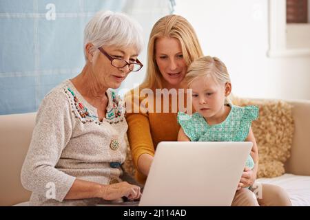 Ein paar Familienfotos im digitalen Zeitalter. Eine kleine Aufnahme einer jungen Frau und ihrer Tochter, die drinnen mit einem Laptop sitzen. Stockfoto