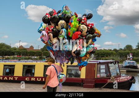 Ein junger Mann, der mit Helium gefüllte Folienballons mit Comicfiguren im Tourismusziel Stratford-upon-Avon, England, verkauft. Stockfoto