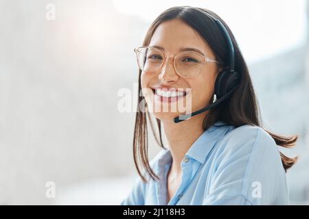 Überlasst mir die harte Arbeit. Aufnahme einer attraktiven jungen Verkäuferin, die allein im Büro sitzt und ein Headset trägt. Stockfoto