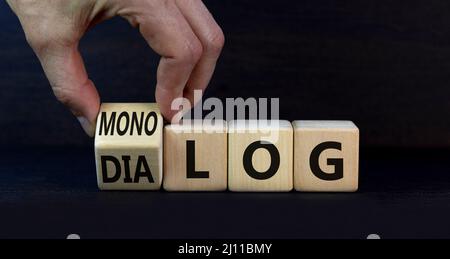 Geschäftsmann dreht Holzwürfel und ändert das deutsche Wort Monolog - Monolog auf Englisch in Dialog - Dialog auf Englisch. Schöner grauer Hintergrund. Stockfoto