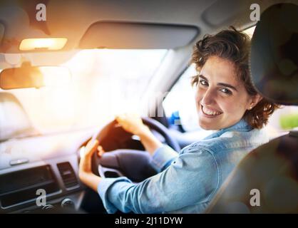 Du bist jetzt auf dem Fahrersitz. Porträt einer glücklichen jungen Frau, die ein Auto fährt. Stockfoto