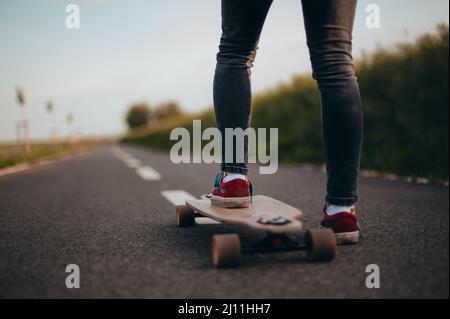 Frau steht auf einem Longboard ein Bein.Copy Space, Poster, Banner, anonyme Fotografie. Gesichtslos . Sonniger Tag . Stockfoto