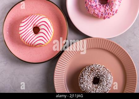 Drei glasierte Donuts liegen auf hohen rosafarbenen Tellern Stockfoto