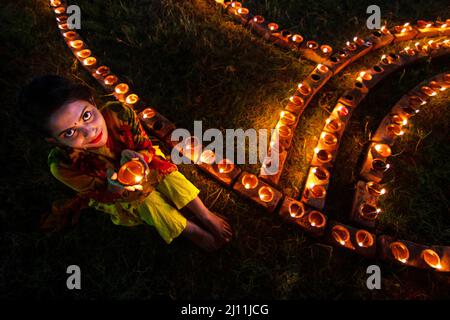 Hinduistische Anhänger zünden irdene Lampen an einem Rangoli an, einem Rahmen aus dekorierten Mustern auf einem Feld, als Teil der Diwali-Feierlichkeiten in Narayanganj, Bangladesch. Viele leichte Öllampen oder Kerzen symbolisieren den Sieg des Lichts über die Dunkelheit, und im Rahmen der Feierlichkeiten werden Feuerwerke aufgesetzt. Dieses Fest findet jedes Jahr in Übereinstimmung mit dem hinduistischen Mondkalender statt. Das Wort 'Diwali' selbst leitet sich vom Sanskrit-Wort 'deepavali' ab, was 'Leuchtereien' bedeutet, daher ist es auch als das Fest der Lichter bekannt. Diwali wird in der Regel durch Geselligkeit und Austausch von Geschenken mit f gefeiert Stockfoto