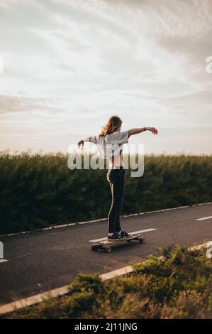 Mädchen reitet ein Longboard mit ausgestreckten Armen und genießt eine freie Fahrt. Sonniger Tag, Poster, Longboard Day vertikales Banner Stockfoto