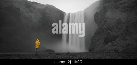 Skogafoss Wasserfall in Island, Langzeitbelichtung, einsamer Typ mit gelbem Regenmantel Stockfoto