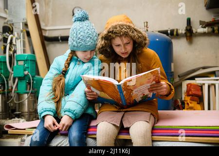 Dnipro, Ukraine - 21. März 2022: Eine Gruppe von Kindern versteckt sich während eines Luftangriffs im Keller. Kinder lesen ein Buch. Stockfoto