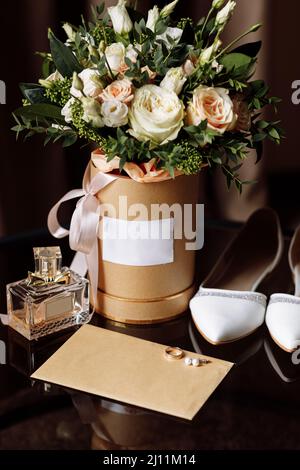 Hochzeitsaccessoires auf einem Holzhintergrund. Weiße Hochzeitsschuhe. Brautstrauß mit rosa Blüten und Grüntönen. Eheringe, weiße Brautschuhe, verheiratet Stockfoto