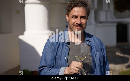 Glücklicher Mann, der draußen Wein trinkt und Weinglas hält, lächelnd. Weinprobe in Weinrebe. Porträt des reifen Alters, mittleren Alters, mittleren Erwachsenen Mann im Jahr 50s. Stockfoto