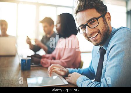 Optimistischer Blick auf die Zukunft seiner Karriere. Porträt eines Geschäftsmannes mit einem digitalen Tablet und seinen Kollegen im Hintergrund. Stockfoto