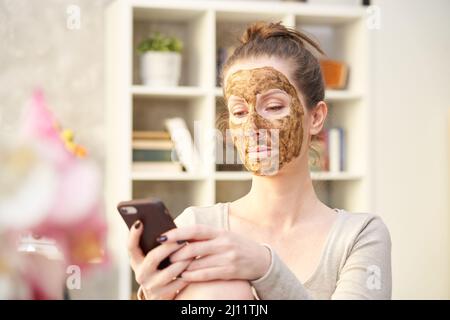 Frau kosmetische Gesichtshaut Pflege. Frau in der Haut Gummi Peeling Gesicht Schönheitsmaske mit Telefon im Home Office. Stockfoto