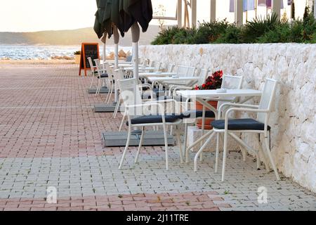 Sitzgelegenheit im Sommer in Erholung am Meer. Weißer Tisch und Sessel auf der Außenterrasse des Sommercafés. Restaurantbetrieb erwartet die Besucher. Stockfoto