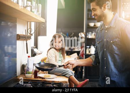 Papa macht die besten Pfannkuchen aller Zeiten. Aufnahme eines Vaters und einer Tochter, die zusammen Pfannkuchen backen. Stockfoto