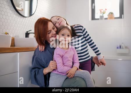 Mutter von zwei kleinen Mädchen umarmt sie im Badezimmer zu Hause. Stockfoto