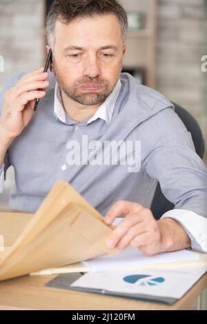 Geschäftsmann mit Computer, der im Büro auf dem Telefon anruft Stockfoto