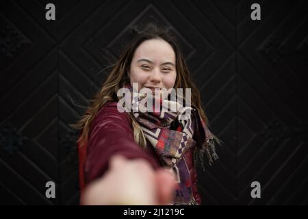 Junge Frau mit Down-Syndrom beim Blick auf die Kamera auf schwarzem Hintergrund Stockfoto