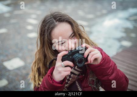 Junge Frau mit Down-Syndrom mit Kamera in der Stadt im Winter und Blick auf die Kamera. Stockfoto