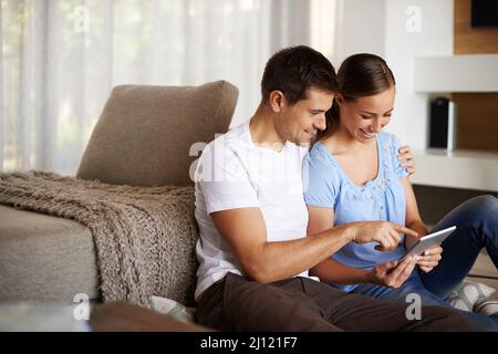 Überlassen Sie uns die eigenen Geräte. Ein liebevolles junges Paar, das in seinem Wohnzimmer ein Tablet benutzt. Stockfoto