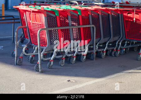 Abbildung von einigen roten Kunststoffwagen, die sich in einem ausgewiesenen Bereich des Parkplatzes eines Gewerbegebiets befinden Stockfoto