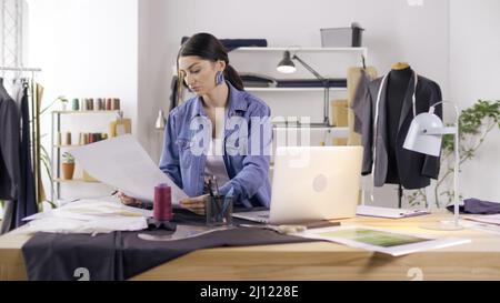 Ein professioneller Modedesigner erstellt in einem Fashion Business Startup Studio eine neue Kollektion, zeichnet, arbeitet mit Skizzen mit einem Laptop. Konzept von H Stockfoto