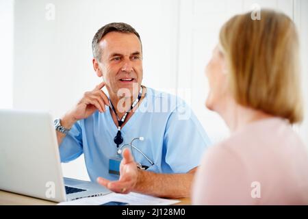 Reifer Arzt im Gespräch mit einer Patientin, die am Schreibtisch sitzt. Porträt einer reifen Ärztin im Gespräch mit einer Patientin, die am Schreibtisch sitzt. Stockfoto