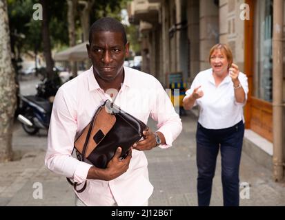 Mann, der mit einer gestohlenen Handtasche von einer älteren Frau davonläuft Stockfoto