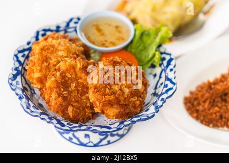 Frittierte Garnelenkuchen auf einem schönen Teller mit Pflaumensoße, Nahaufnahme Bild von frittierten Garnelenkuchen mit verschwommenen anderen Lebensmitteln auf weißem Hintergrund, ein Stockfoto
